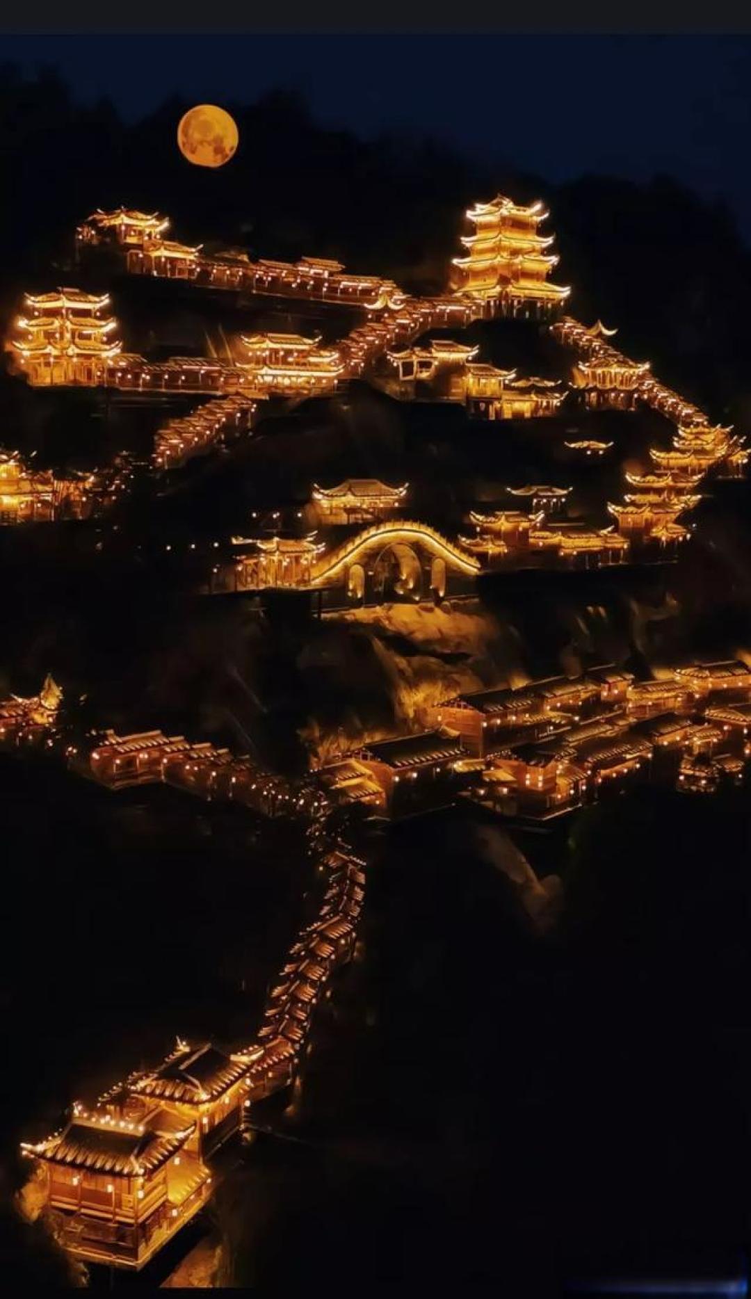 Wangxian Valley illuminated at night with warm golden lights cascading down the cliff face, creating a magical vertical village of light
