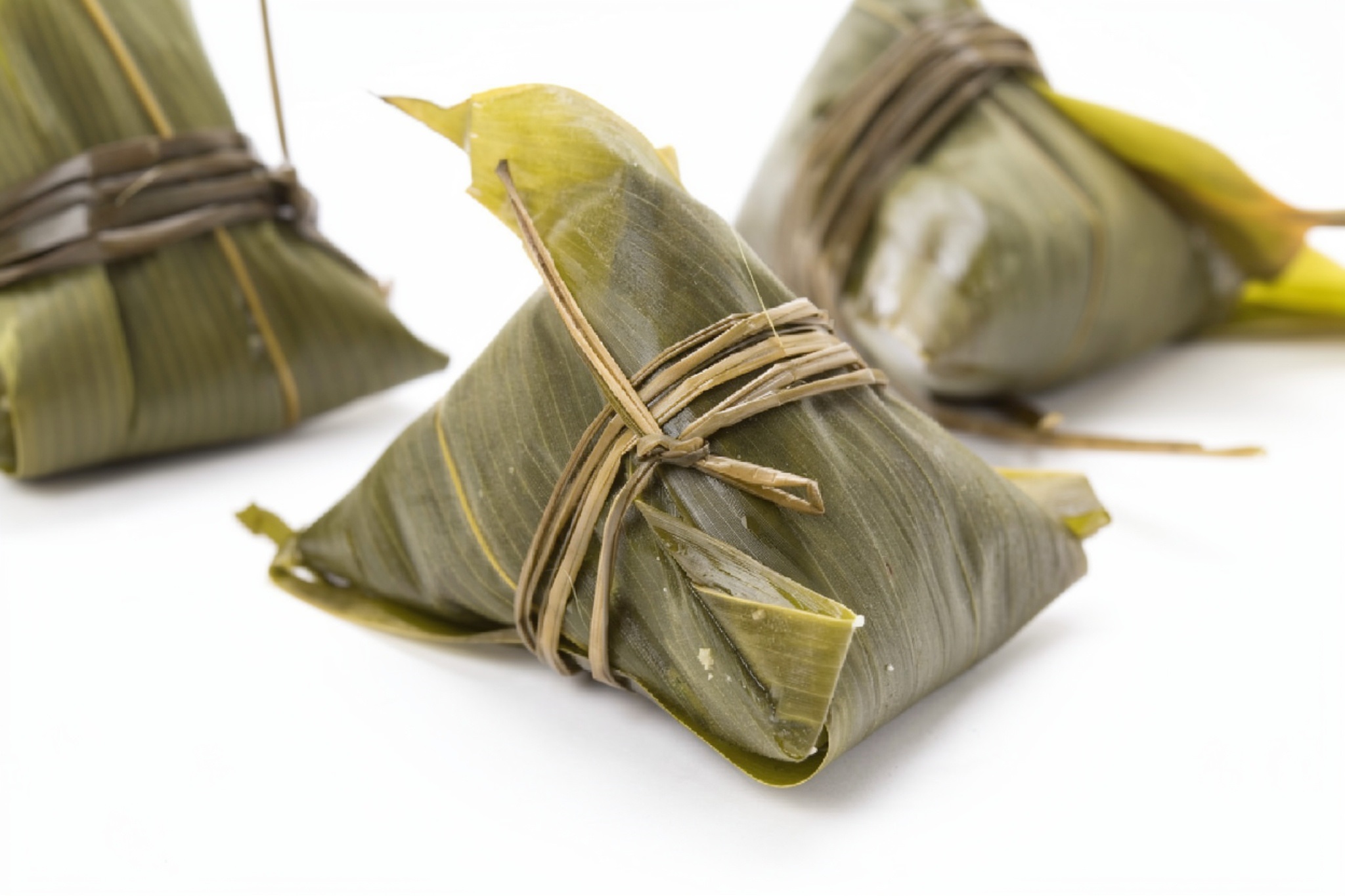 Freshly steamed zongzi wrapped in bamboo leaves, some cut open to reveal glutinous rice and savory fillings